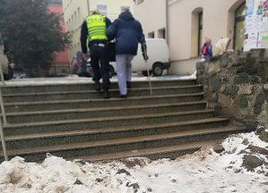 Policjant pomaga wejść seniorowi po oblodzonych schodach